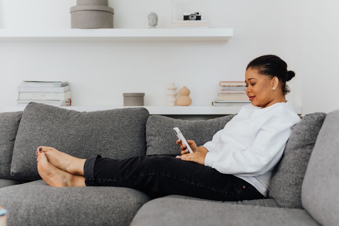 A woman relaxes on her sofa, looking something up on her phone.