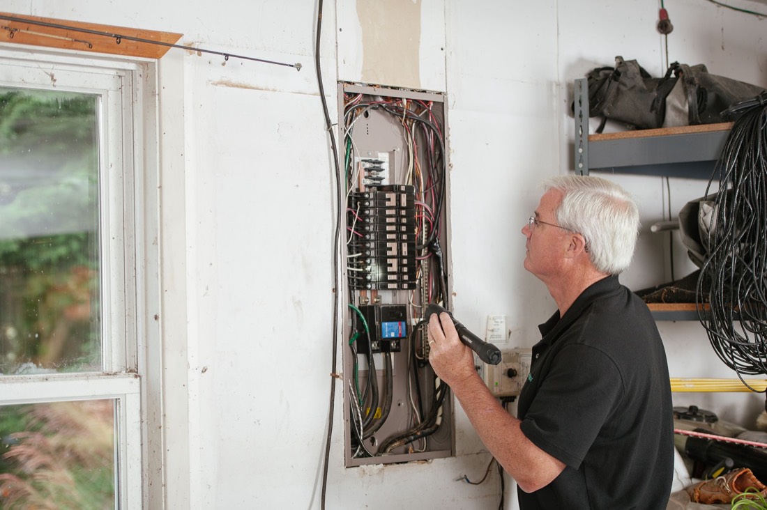 An electrician with white hair checks a home's breaker panel.