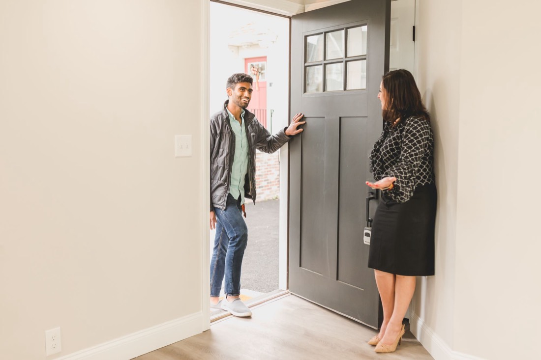 A real estate agent opens the front door of a house for a visitor.
